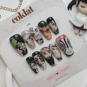 Puede incluir: Un conjunto de diseños de uñas personalizados con ilustraciones de personajes de anime. Las uñas muestran obras de arte detalladas de varios personajes en colores como negro, verde, rojo y blanco. La marca "cokolat nails" es visible.