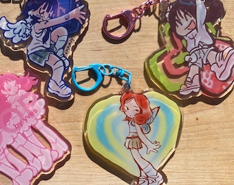 May include: Four colorful anime-style character keychains with different designs. Each keychain features a different character with a unique pose and background. The keychains are made of clear acrylic and have metal rings for attaching to keys or bags.