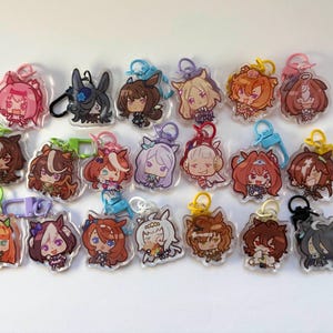Könnte beinhalten: Eine Sammlung von Schlüsselanhängern mit Anime-Charakteren. Jeder Schlüsselanhänger zeigt einen anderen Charakter mit einzigartigen Haarfarben und Outfits. Die Schlüsselanhänger sind aus klarem Acryl gefertigt und haben einen Metallverschluss.