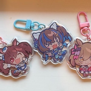 Könnte beinhalten: Drei Schlüsselanhänger aus Acryl mit Anime-Charakteren. Jeder Schlüsselanhänger hat ein anderes Design und einen farbigen Verschluss: rosa, blau und rosa. Die Schlüsselanhänger liegen auf einer weißen Oberfläche.