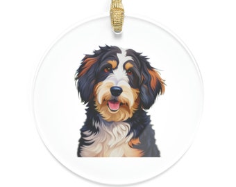 May include: A round glass ornament featuring a cartoon illustration of a black, brown, and white dog with a happy expression. The dog has a long, fluffy coat and is looking directly at the viewer.