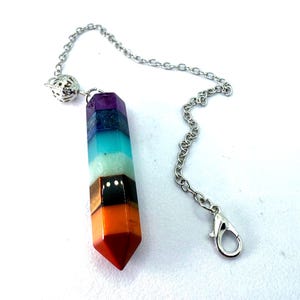 May include: A multi-colored crystal pendulum with a silver chain and clasp. The crystal is a hexagonal shape with layers of purple, blue, turquoise, green, brown, orange, and red. The chain is attached to a decorative silver bead.