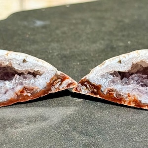 May include: Two halves of a geode, revealing a cavity filled with purple crystals. The outer shell is a mix of white and brown, with a rough texture. The geode is cut open, showing the inner crystalline structure.