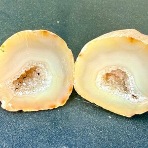 May include: Two halves of a geode, showcasing a natural, organic aesthetic. The interior features a crystalline center, surrounded by layers of creamy white and pale yellow hues. The outer edges display a warm, earthy tone.