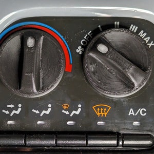 Puede incluir: Un tablero de instrumentos de coche negro con una perilla de control de temperatura, una perilla de velocidad del ventilador y una fila de botones para los controles de los asientos y el parabrisas. La perilla de temperatura está configurada en el medio, la perilla de velocidad del ventilador está configurada en la configuración más alta y los botones de los asientos y el parabrisas están todos apagados. El texto "A/C" es visible en el tablero.