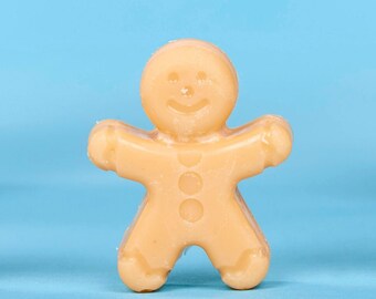 Puede incluir: Tres figuritas de hombre de jengibre se encuentran frente a dos árboles de Navidad en miniatura. Los hombres de jengibre están hechos de una masa de galletas de azúcar marrón claro y tienen una cara simple y sonriente.