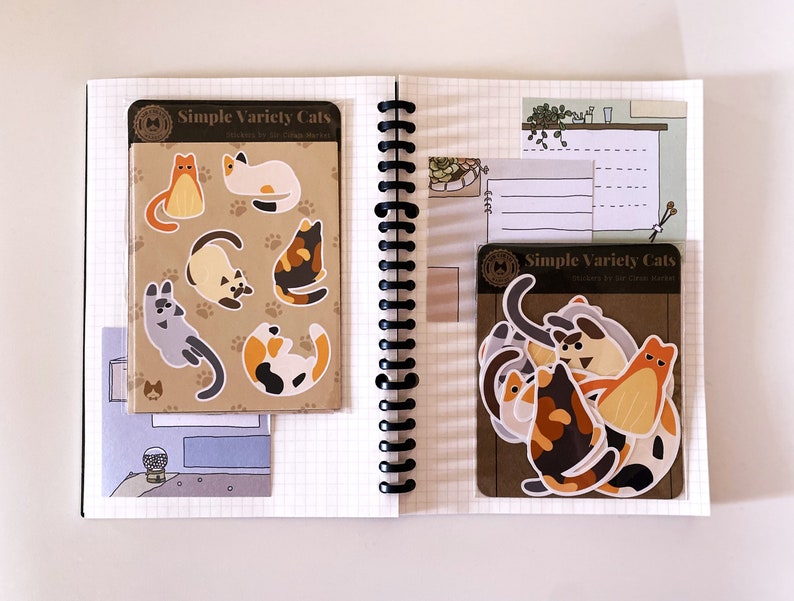 May include: Two sheets of stickers featuring illustrations of cats in various poses. The stickers are on a brown background with the text "Simple Variety Cats" and "Stickers by the Cat Market".