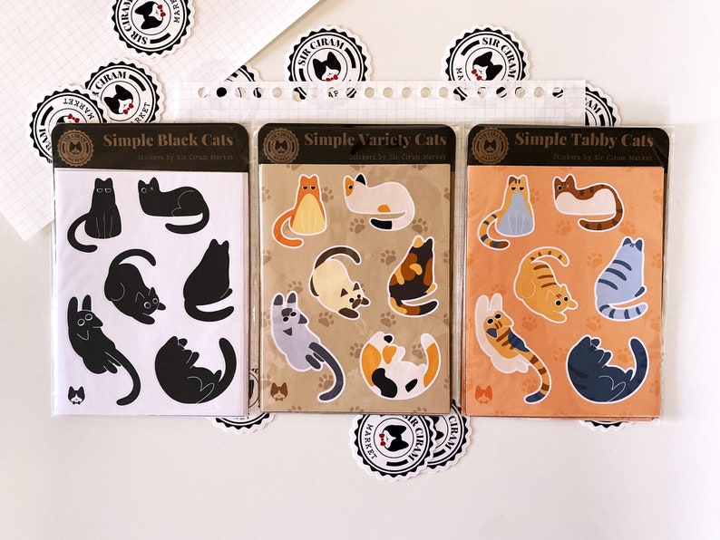 May include: Three packs of cat stickers featuring different cat designs. The first pack has black cats in various poses. The second pack has a variety of cats in different colors and poses. The third pack has tabby cats in different poses. Each pack has the text "Simple" and the type of cat on the front.