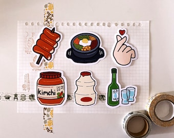May include: A set of seven Korean food themed stickers. The stickers feature a jar of kimchi, a bottle of soju, two shot glasses, a container of yogurt, a bowl of bibimbap, a skewer of Korean street food, and a hand making the Korean heart sign.
