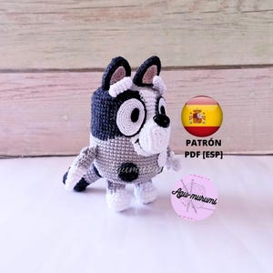 Puede incluir: Juguete de amigurumi tejido a crochet de un perro gris y negro con detalles blancos. El juguete está sentado sobre una superficie de madera. La imagen incluye el texto "PATRÓN PDF [ESP]".