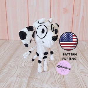 Puede incluir: Un perro dálmata de ganchillo, blanco con manchas negras, ojos grandes y nariz negra. La imagen incluye un gráfico redondo con la bandera estadounidense y el texto "PATTERN PDF [ENG]" y un logotipo rosa.