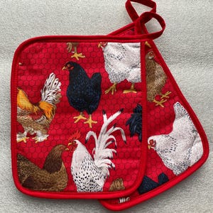 May include: A pair of red quilted pot holders with a chicken and rooster pattern. The pot holders have a loop for hanging.