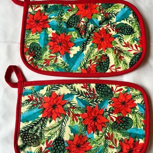 May include: A pair of red and white pot holders with a Christmas poinsettia and pine cone design.
