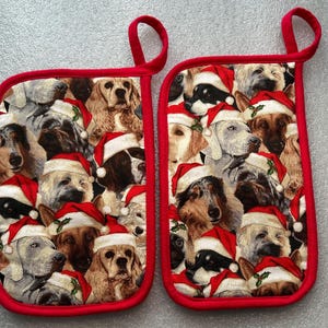 May include: Two rectangular oven mitts with a red trim and hanging loop. The mitts are covered in a pattern of various dog breeds wearing Santa hats. The background is a light gray color.