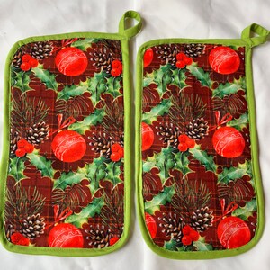 May include: A pair of green and brown Christmas-themed pot holders with a red and white ornament pattern.