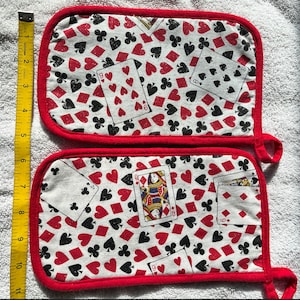 May include: A pair of red and white pot holders with a playing card design. The pot holders feature a variety of playing cards, including hearts, diamonds, clubs, and spades. The pot holders are made of a cotton fabric and have a red trim.