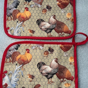 May include: Two matching pot holders with a red trim and loop. The fabric features a beige background with a repeating pattern of roosters, hens, and chicks. The design includes a chicken wire pattern.