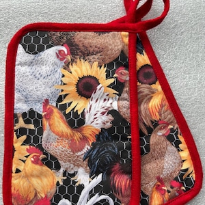 May include: A double-sided quilted oven mitt featuring a black background with a white chicken wire pattern. The fabric displays various chickens, roosters, and yellow sunflowers. The edges are finished with red fabric trim and a red hanging loop.