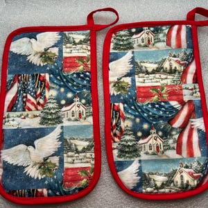 May include: Pair of oven mitts with a red trim and hanging loop. The mitts feature a patchwork design with images of the American flag, a white dove, a church, and a winter landscape. The background is a starry blue.