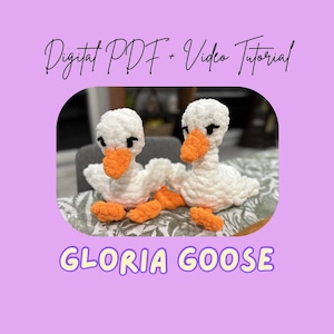 May include: Two handmade white crochet geese with orange beaks and feet. The geese are positioned on a patterned surface, with the text "Digital PDF + Video Tutorial" and "Gloria Goose" in the image.