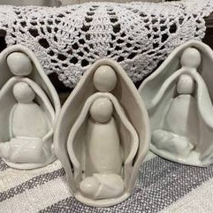 May include: Three white ceramic nativity scene figurines. Each figurine depicts Mary, Joseph, and the baby Jesus. The figurines are in a simple, modern style.
