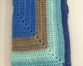 Puede incluir: Una manta de ganchillo rectangular con un patrón de cuadrado dentro de otro cuadrado y bandas concéntricas de color. Los colores del hilo incluyen azul marino intenso, azul real brillante, beige neutro y verde menta suave, en punto vareta.