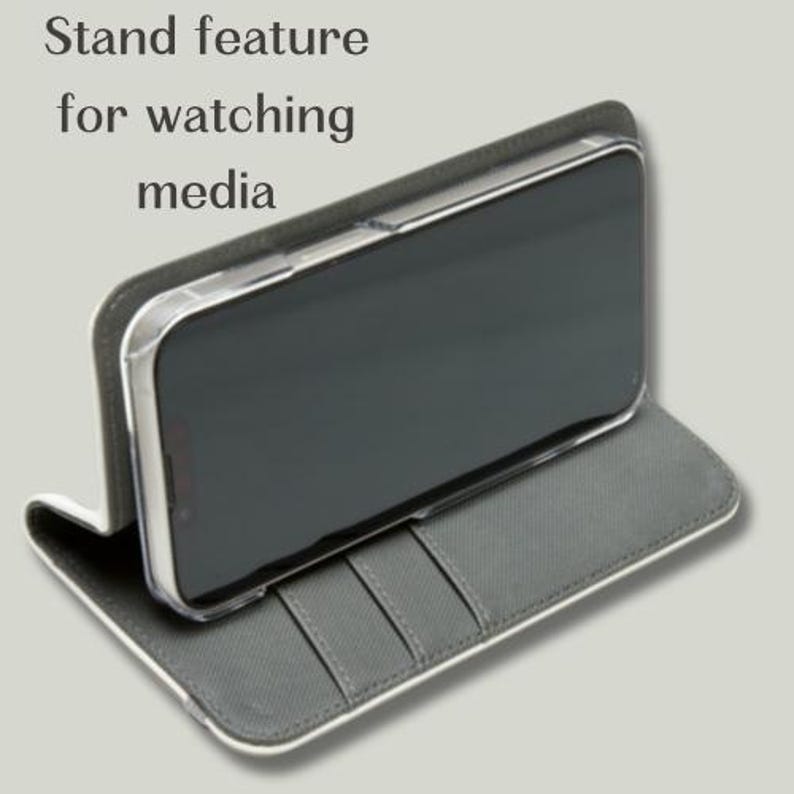 May include: A gray phone case with a white border, featuring a stand function for media viewing. The case holds a smartphone with a dark screen. The case has slots for cards. The text "Stand feature for watching media" is visible.