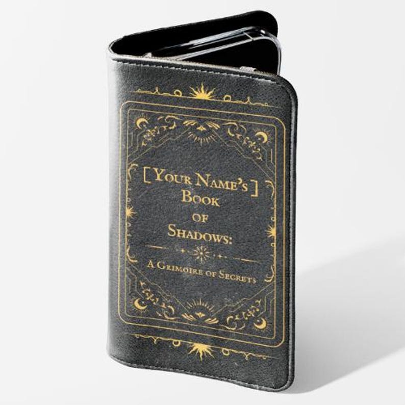 May include: Black phone case with a gold-colored decorative frame and text that reads "[Your Name's] Book of Shadows: A Grimoire of Secrets". The case is designed to hold a phone.