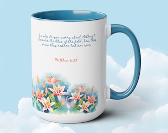 May include: White ceramic mug with a blue interior and handle. The mug features a floral design with lilies and text from Matthew 6:28. The text reads, "So why do you worry about clothing? Consider the lilies of the field, how they grow: they neither toil nor spin."