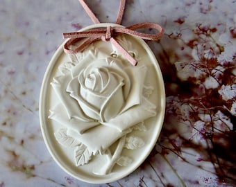 May include: A white ceramic rose pendant with a pink suede cord. The rose is detailed with a raised design and is oval shaped.