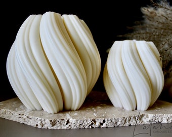May include: Two white, swirl-shaped candles on a stone base. The larger candle is in the background and the smaller candle is in the foreground. The candles are made of a smooth, white wax.