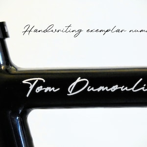 Peut inclure: Gros plan sur un cadre de vélo noir avec le nom "Tom Dumoulin" en écriture blanche. Le texte "Handwriting exemplar number 1" est également visible en cursive.