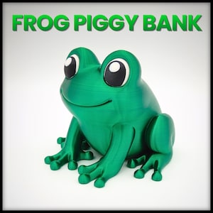 Könnte beinhalten: Eine grüne, froschförmige Spardose mit großen, ausdrucksstarken Augen und einem lächelnden Mund. Der Text "FROG PIGGY BANK" ist grün über dem Frosch dargestellt. Der Frosch sitzt auf einer weißen Oberfläche.