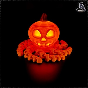 May include: Glowing orange Halloween pumpkin with carved eyes, nose, and mouth, emitting a warm light. The pumpkin sits atop an orange, tentacle-like base, all against a black background. A festive, illuminated decoration.