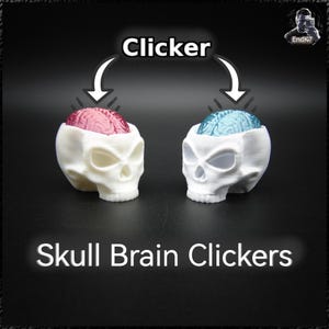 Puede incluir: Dos clickers blancos con forma de calavera, uno con un cerebro rosa y otro con un cerebro azul. La palabra "Clicker" está encima de las calaveras, y "Skull Brain Clickers" debajo. El fondo es negro.