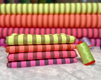 May include: Stacks of colorful striped fabric in shades of yellow, orange, pink, and purple. A spool of green thread with a red base sits nearby. The fabric is likely for sewing or crafting projects.