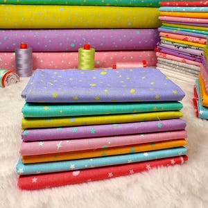 May include: A stack of colorful fabric squares in various shades, including red, blue, pink, purple, yellow, and green. Each fabric piece is decorated with a star and dot pattern. Rolls of matching fabric and spools of thread are in the background.