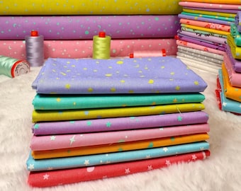 May include: A stack of colorful fabric squares in various shades, including red, blue, pink, purple, yellow, and green. Each fabric piece is decorated with a star and dot pattern. Rolls of matching fabric and spools of thread are in the background.
