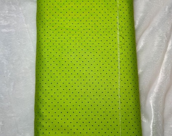 May include: A roll of bright green fabric with a repeating pattern of small, dark blue polka dots. The fabric is tightly rolled and appears to be made of a soft material. The background is a white, textured surface.