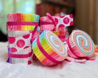 May include: Stacks of colorful fabric rolls, bound with pink ribbon. The fabric displays a rainbow of hues, with floral and polka dot accents. Each roll is neatly packaged, suggesting a craft or quilting supply.