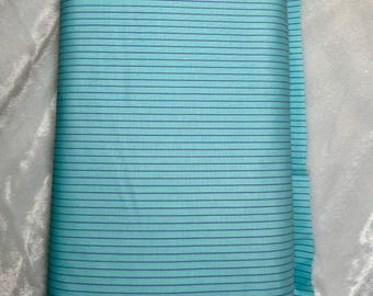 May include: A roll of fabric featuring a light blue background with thin, evenly spaced, dark blue horizontal stripes. The fabric is neatly rolled, showcasing the pattern and texture. The edge of the fabric is visible, revealing the material's thickness and the "TRUE COLORS" text.
