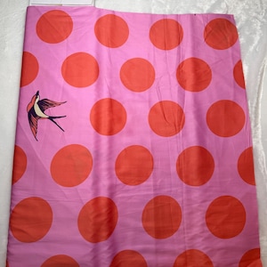 May include: Pink fabric with large orange polka dots and a bird illustration. The fabric is a light pink color with large, evenly spaced orange circles. A bird illustration is on the left side of the fabric.