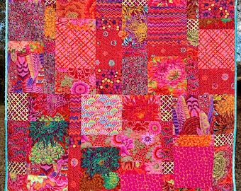 May include: A colorful patchwork quilt with a variety of floral and geometric patterns in shades of pink, red, and green. The quilt is made up of many different squares, each with a unique design.
