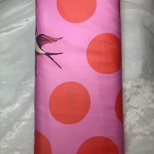 May include: Pink fabric with large orange polka dots and a bird illustration. The fabric is rolled up, showing the pattern of the material. The bird is a stylized design with brown, orange, and purple accents.