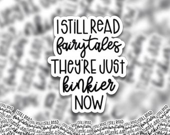 May include: A white sticker with black text that reads "I STILL READ fairytales THEY'RE JUST kinkier NOW." The sticker has a rounded rectangle shape. The background is a blurred pattern of similar stickers.