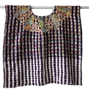 Op de afbeelding: Een donkerpaarse en wit gestreepte tuniek met een geborduurde halslijn met kleurrijke vogels en bloemmotieven. Het kledingstuk heeft een vierkant silhouet met een ruitpatroon aan de onderzoom en verticale strepen over het hele lichaam.