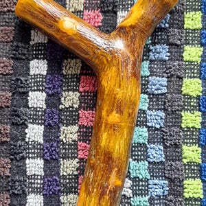 May include: A Y-shaped catapult frame crafted from a single piece of natural wood with a smooth, polished finish. The wood displays a warm, golden-brown colour with visible grain patterns and a sturdy, bifurcated structure for projectile launching.