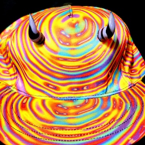 May include: A yellow, blue, red, and green swirl pattern baseball cap with black stitching and two white horns on top.