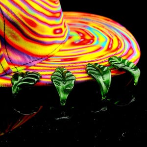 May include: A colorful, psychedelic patterned baseball cap with green leaf-shaped embellishments around the brim.