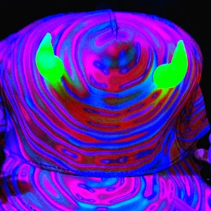 Puede incluir: Una gorra de béisbol de color negro y azul con un patrón de remolino y dos cuernos de diablo verde neón en la parte superior.